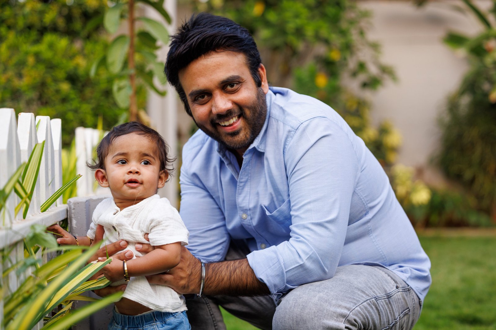 Father holding a baby beside a white fence outdoors