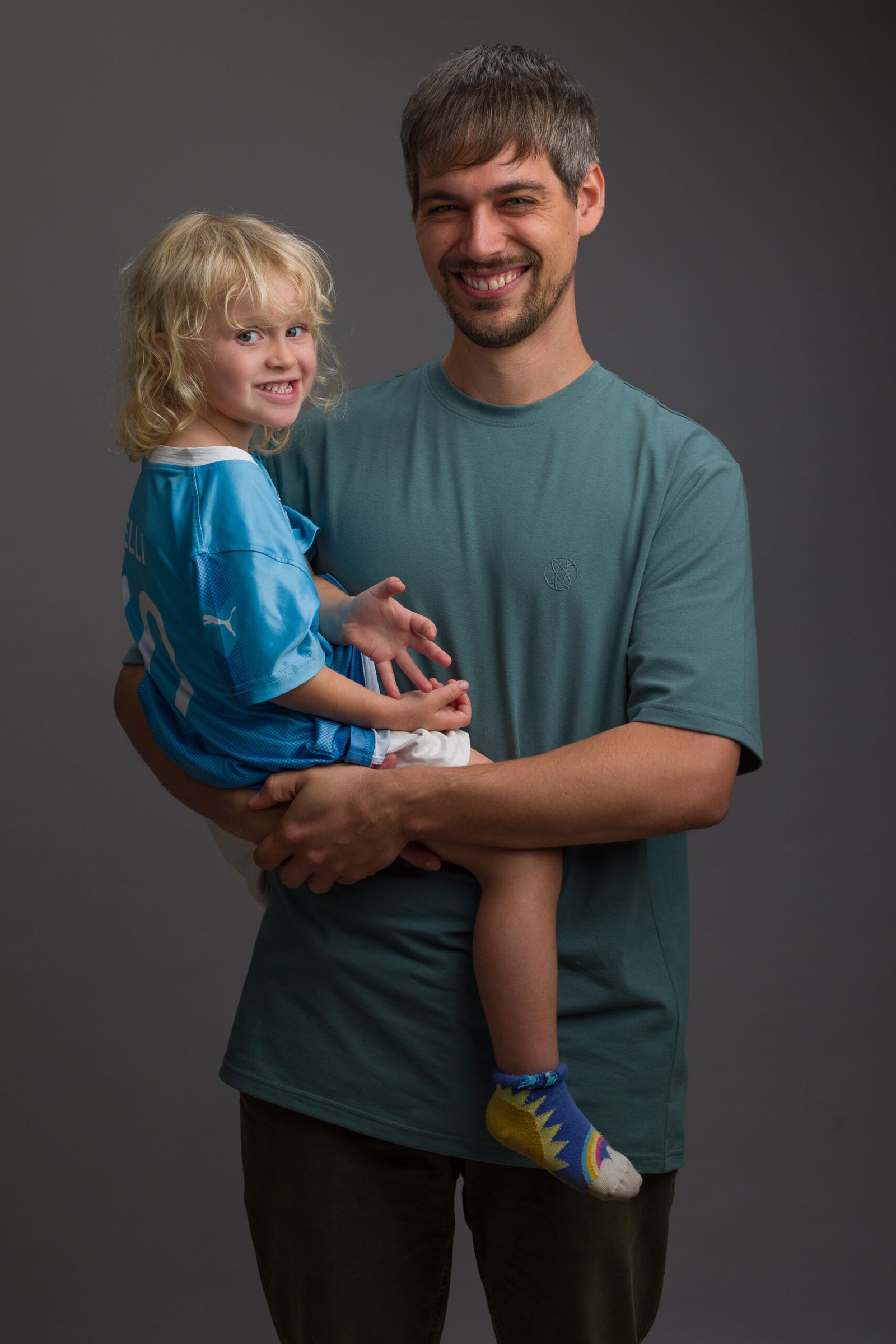Father holding a young child in a blue football shirt during a studio portrait session