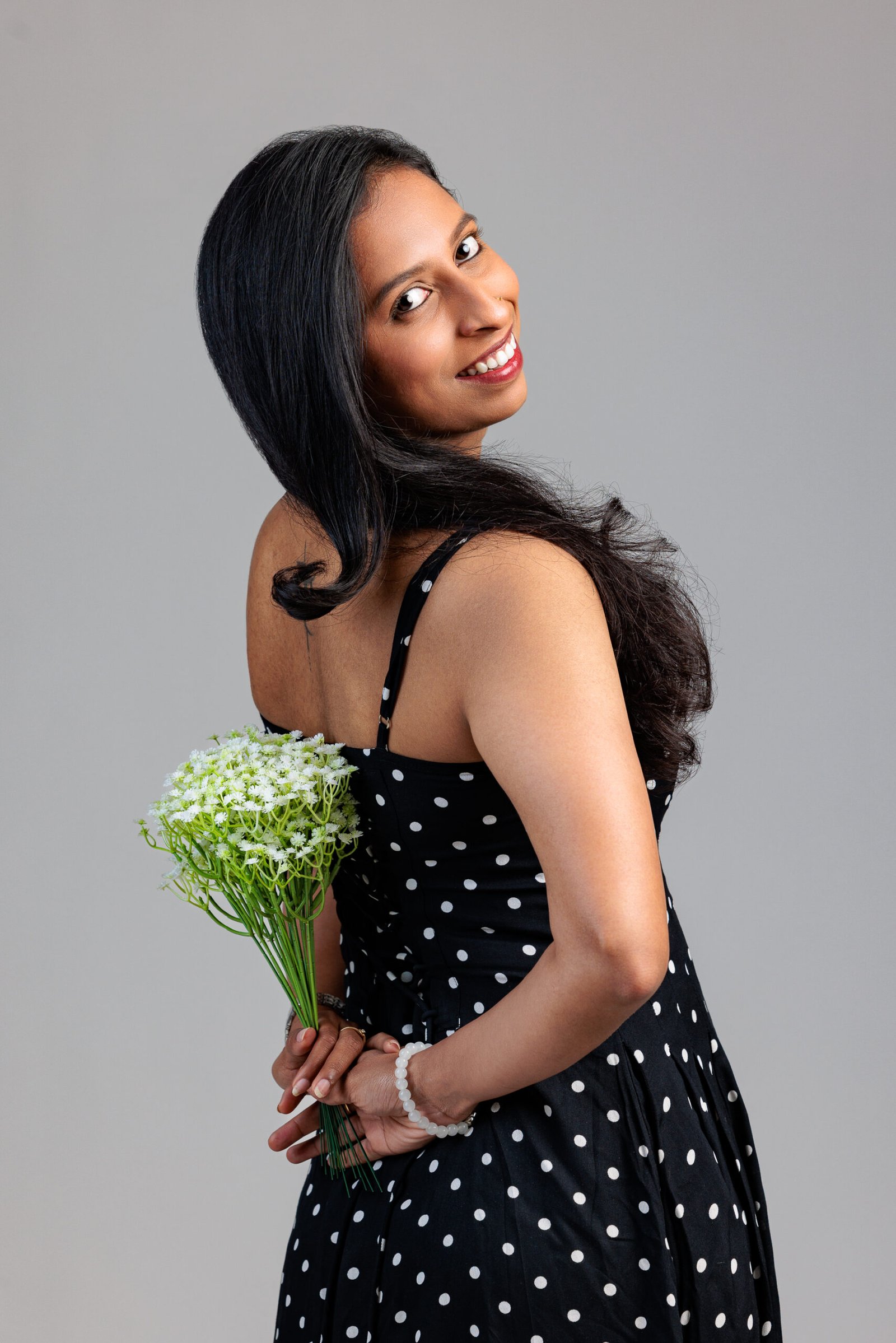 Woman in a black polka-dot dress holding flowers behind her back