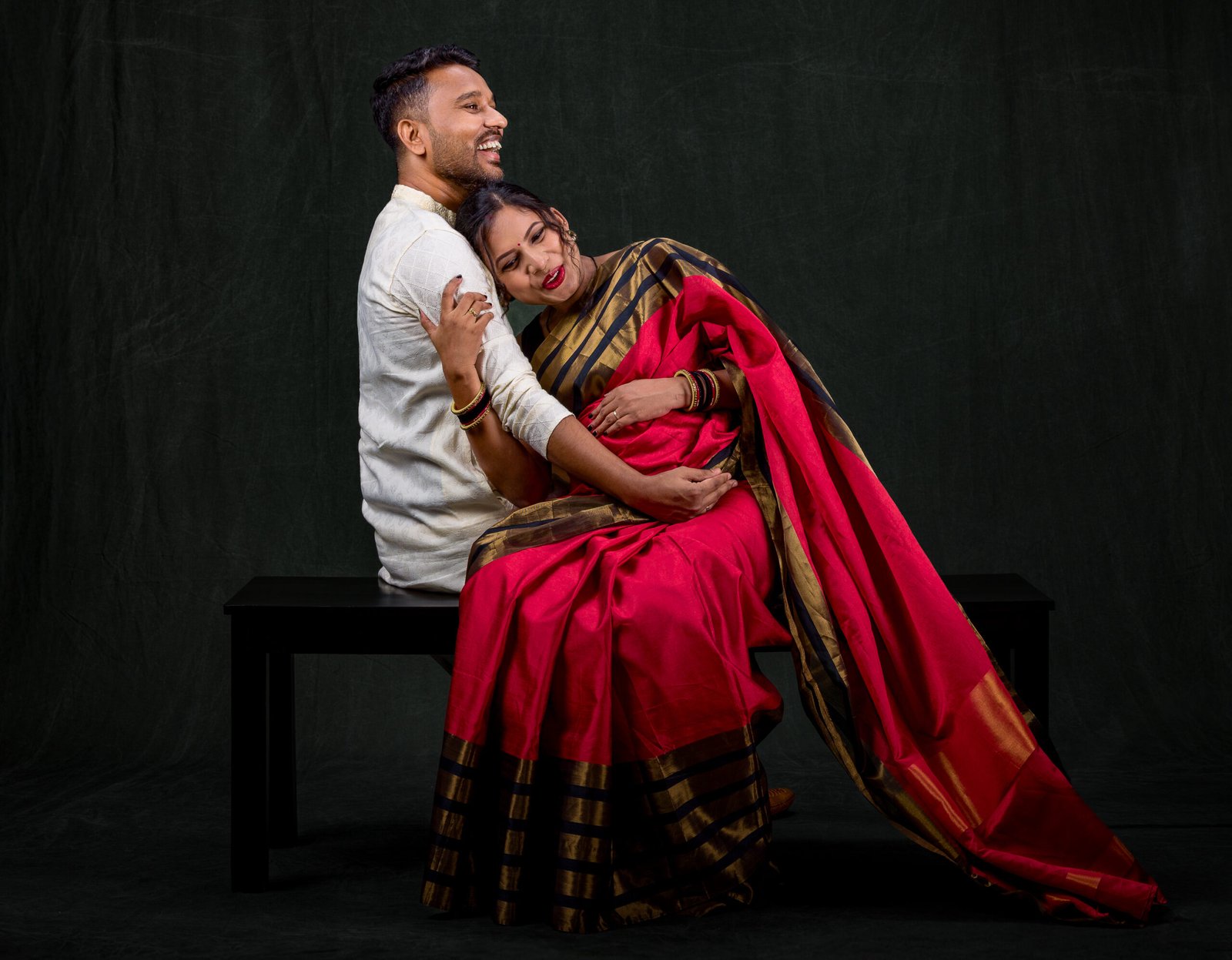 Smiling couple during a maternity portrait session against a dark green background