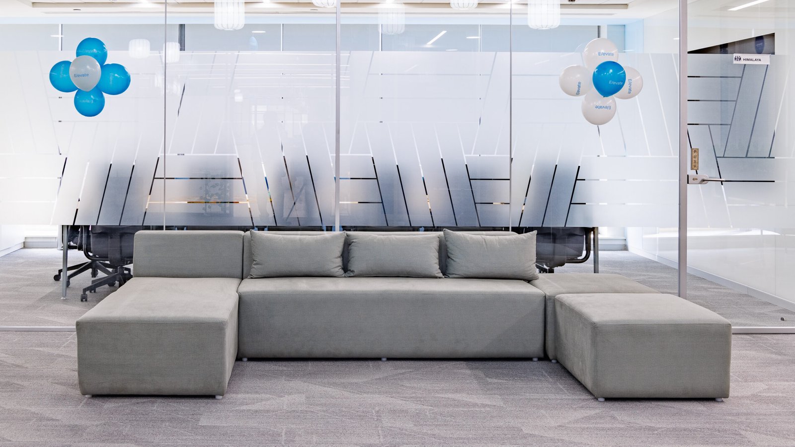 Office lounge with a grey sofa in front of glass meeting rooms