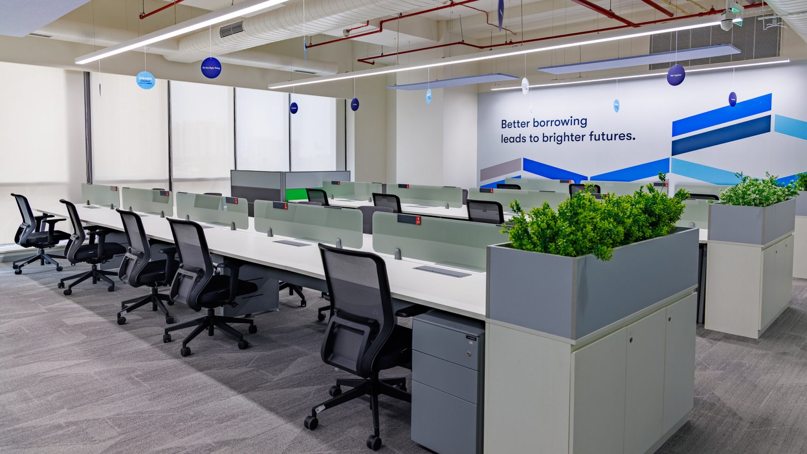 Bright office interior with rows of desks, chairs and green planters
