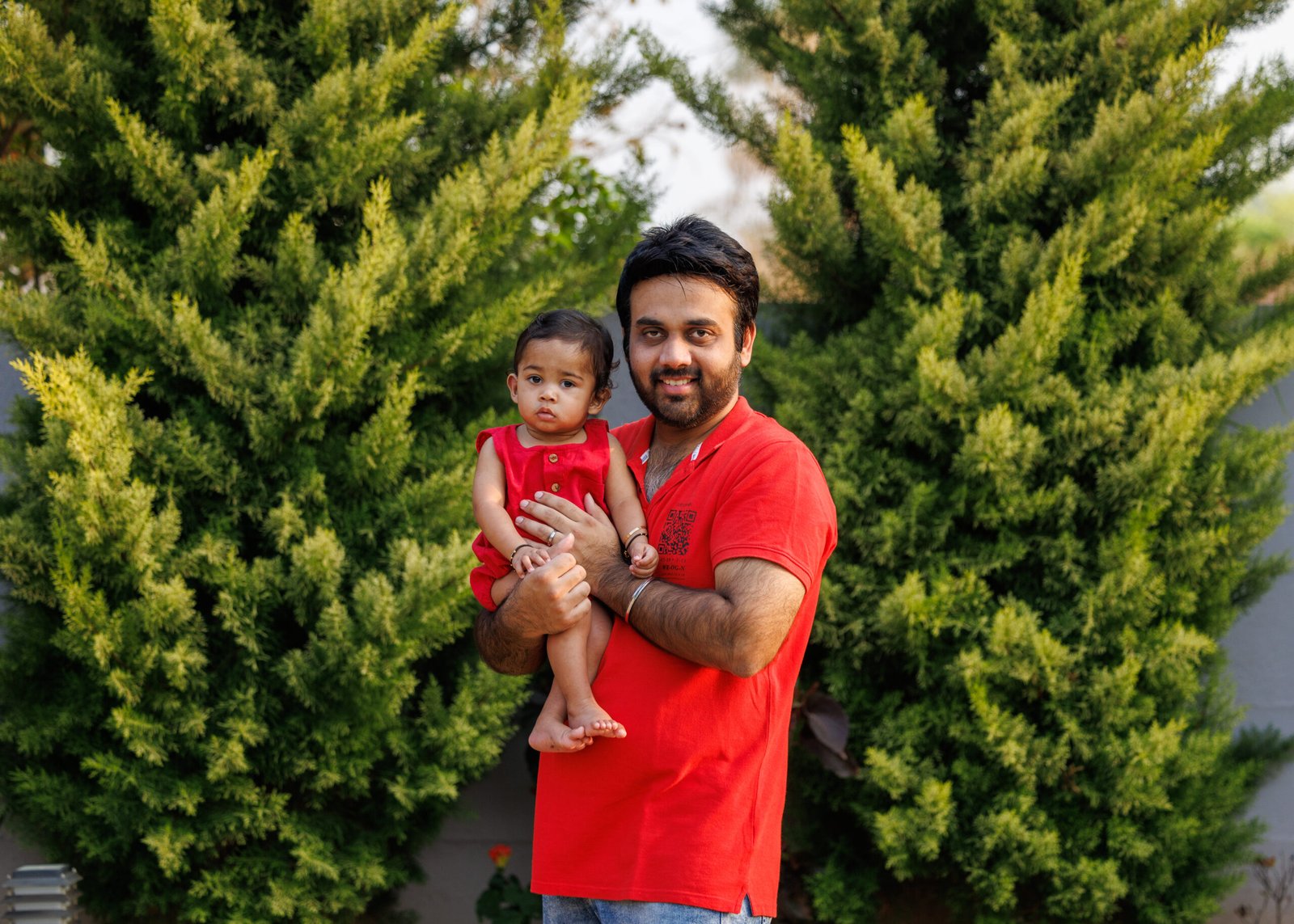 Father in a red shirt holding his baby in a garden