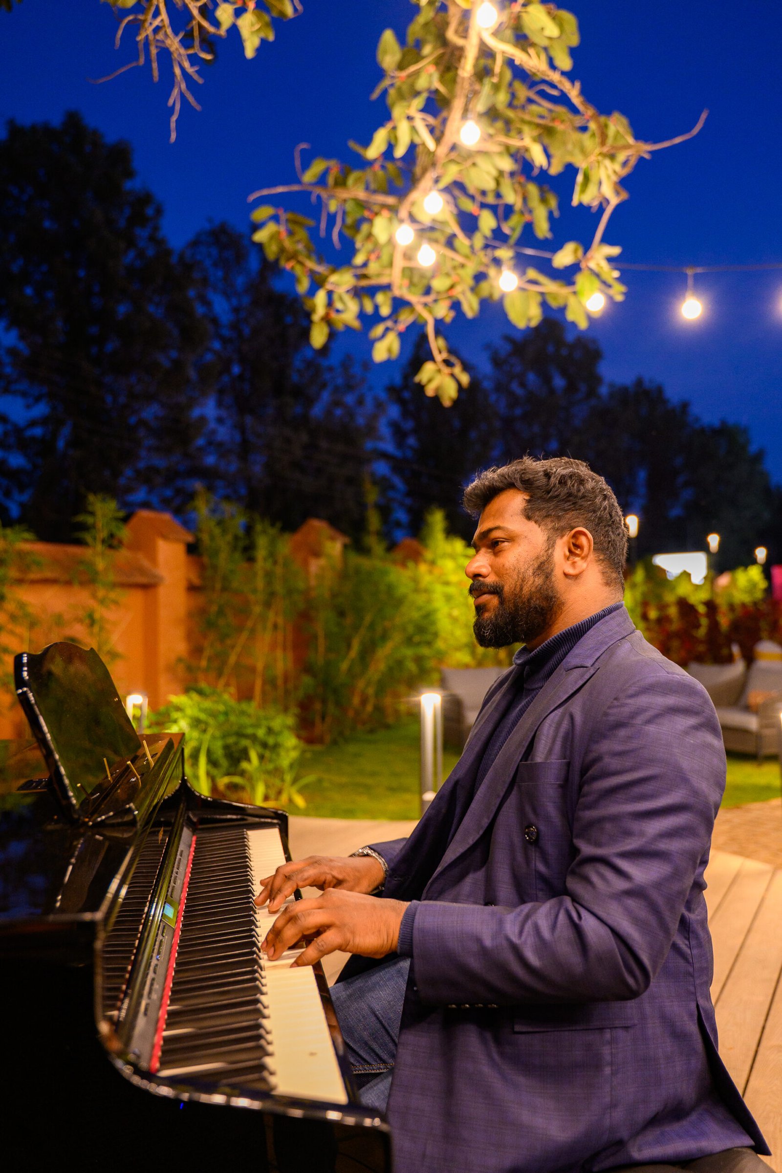 Pianist performing outdoors beneath warm lights at an evening event