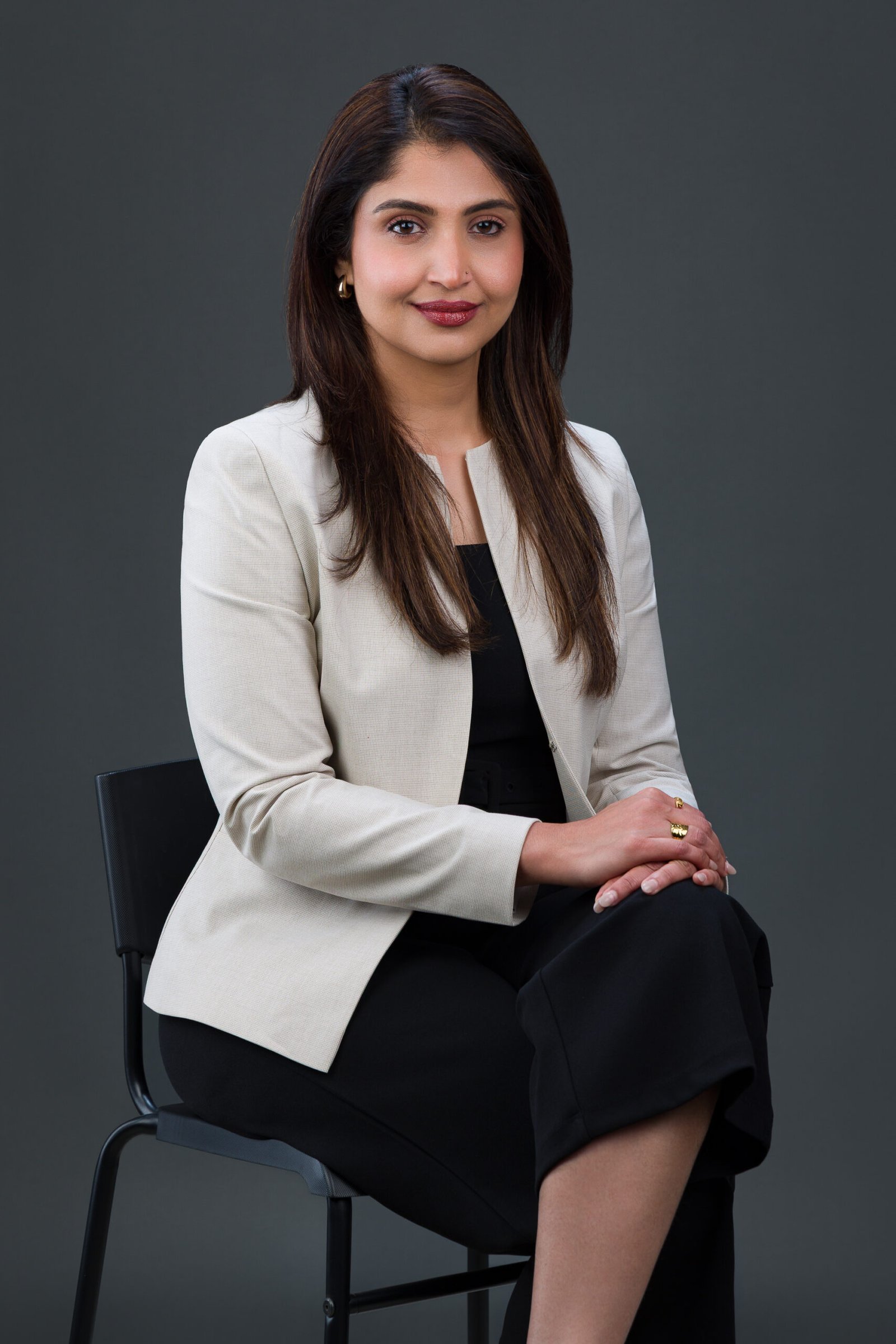 Seated professional portrait of a woman in a light blazer resting her hands on her knee