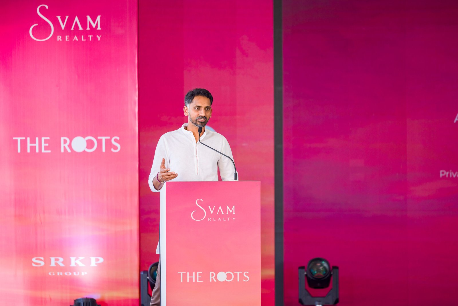 Speaker addressing guests from a lectern against a pink event backdrop