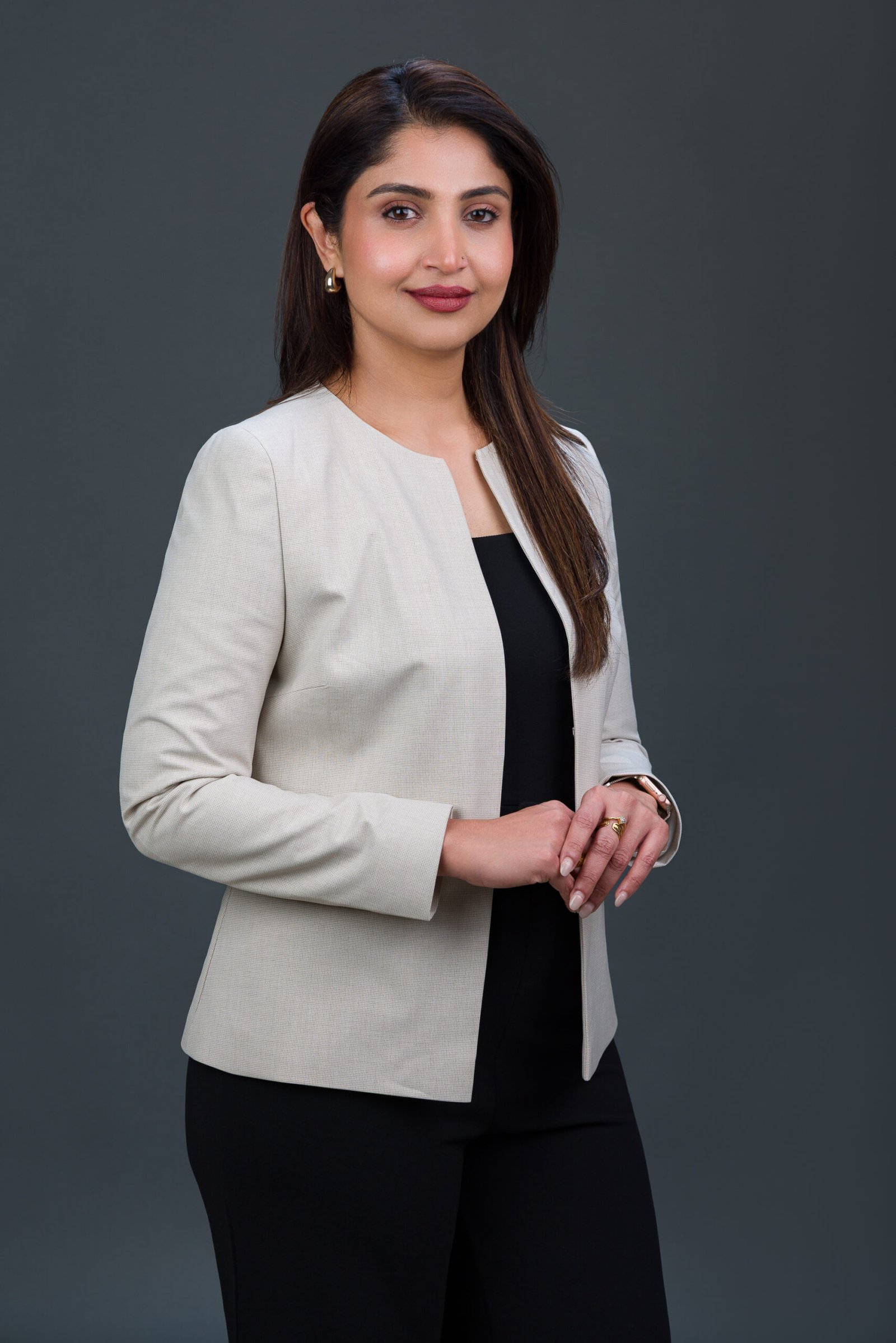 Standing corporate portrait of a woman in a light blazer against a dark studio background