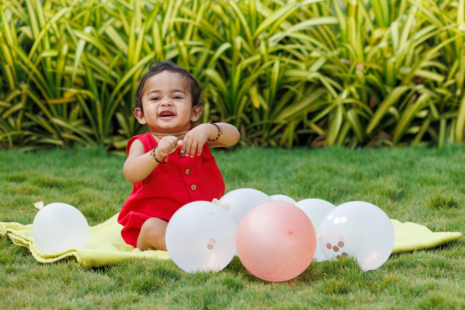 Baby sitting on a lawn beside colourful balloons